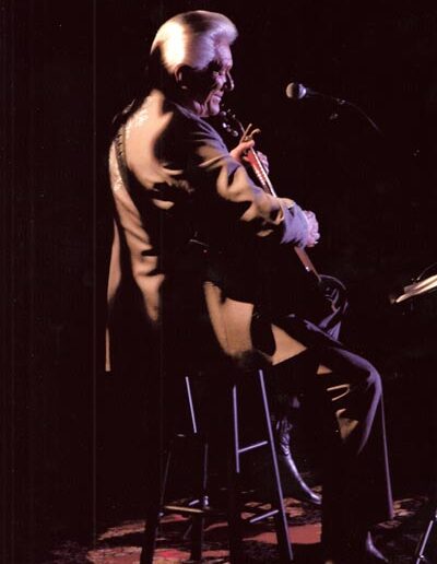 Tommy hunter sitting on a stool and playing on stage.